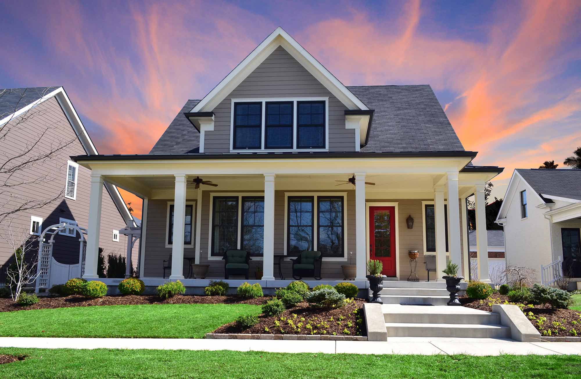 Sunset behind a Single-Family Suburban Craftsman House with Big Front Porch, White Pillars, and a Red Front Door.