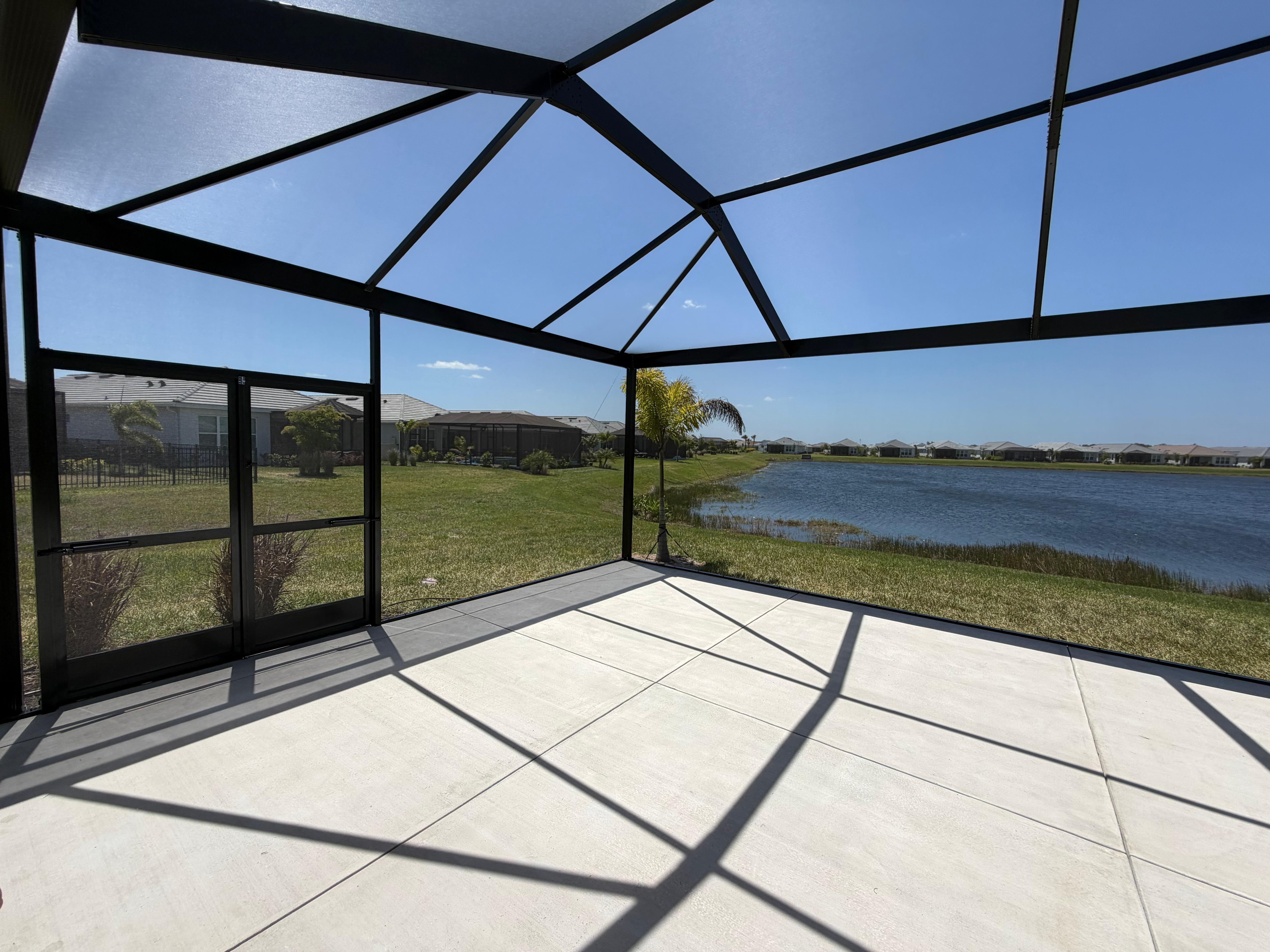 Interior corner view of a Florida bird cage showing the double-door entry, panoramic full-height side walls, and lakefront views. Built in Parrish, FL by Top Tier Home Building Solutions (#CGC1527718).
