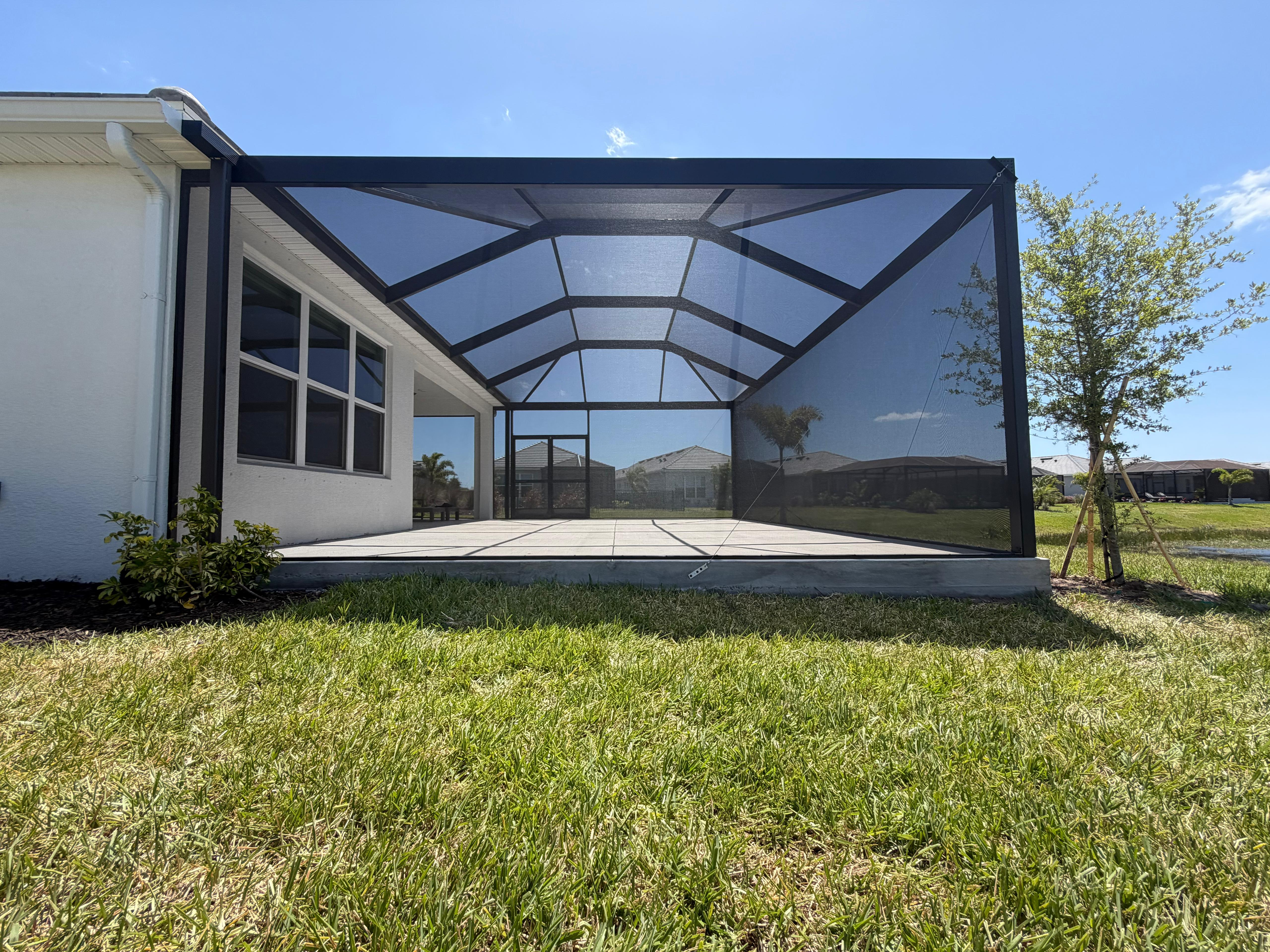 Exterior side view of a recently completed bird cage in Parrish, FL, showing the full mansard roof structure, panoramic side walls without horizontal rails, and integration with a Florida single-story home. Top Tier Home Building Solutions, license #CGC1527718.