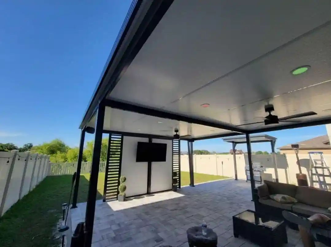 Modern aluminum pergola in Tampa Bay, Florida — black powder-coated frame, solid insulated roof panel, integrated ceiling fans, recessed lighting, outdoor TV, and paver patio. Custom build by Top Tier Home Building Solutions (#CGC1527718).