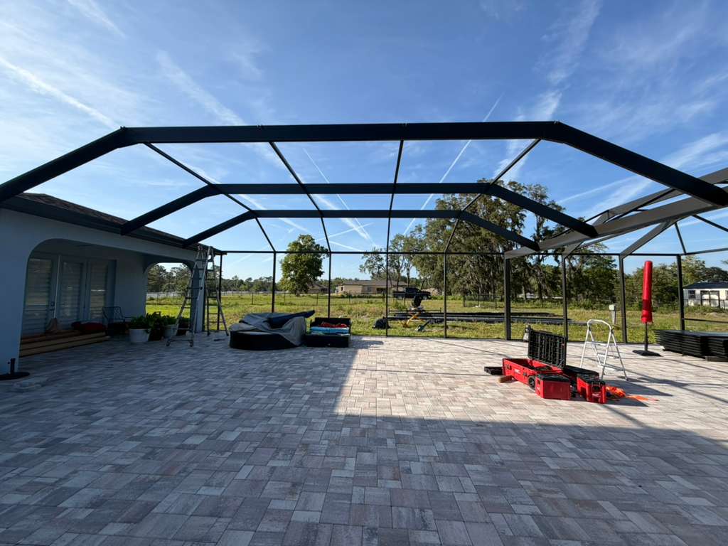 Custom mansard pool cage build in Brooksville, FL — bronze-black aluminum frame complete on a herringbone paver deck, premium build ($80,000–$90,000 tier) by Top Tier Home Building Solutions (#CGC1527718).