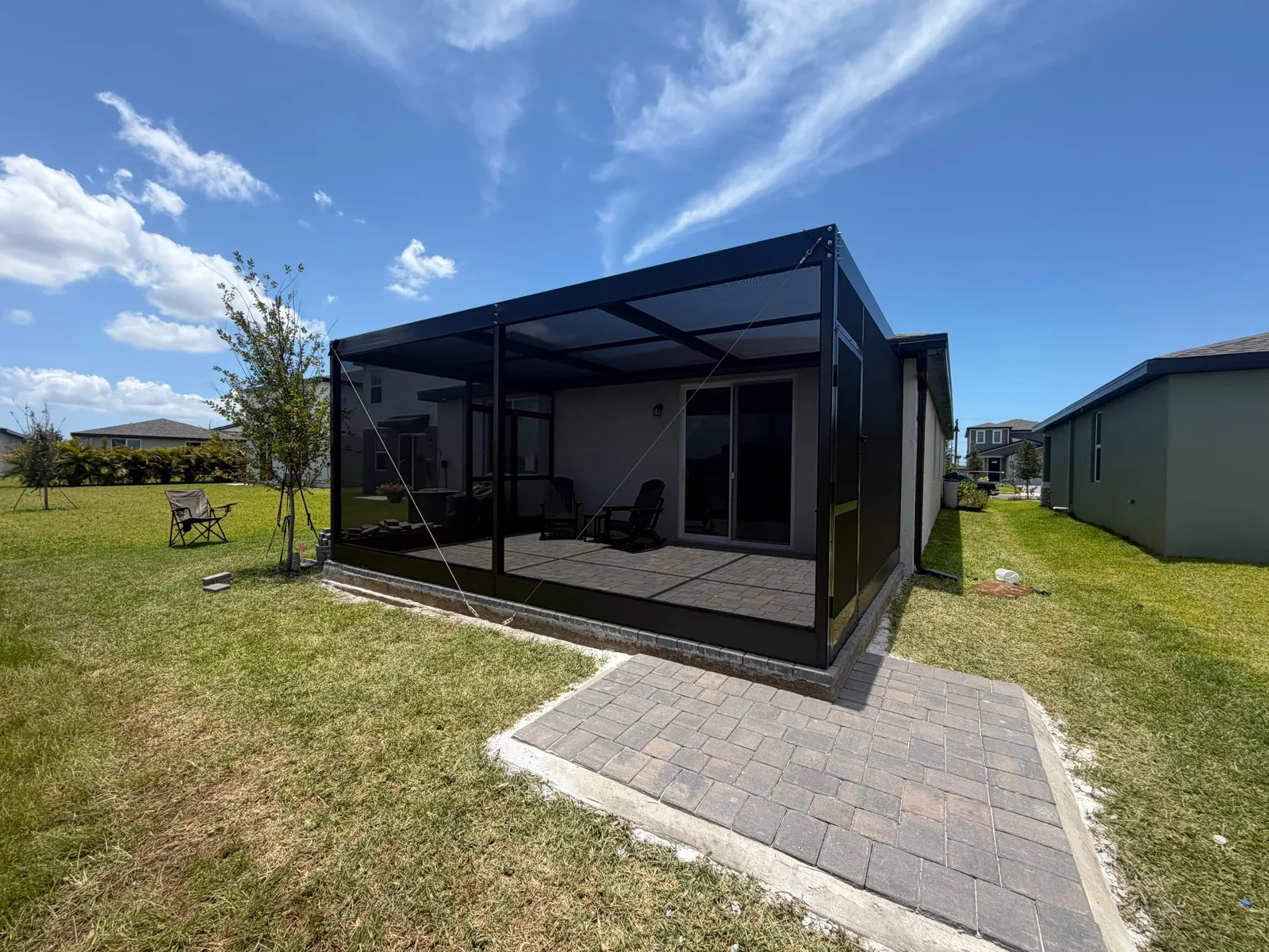 Black screen enclosure built over a brick paver patio with matching paver walkway in Tampa Bay, FL. Top Tier Home Building Solutions, license #CGC1527718.
