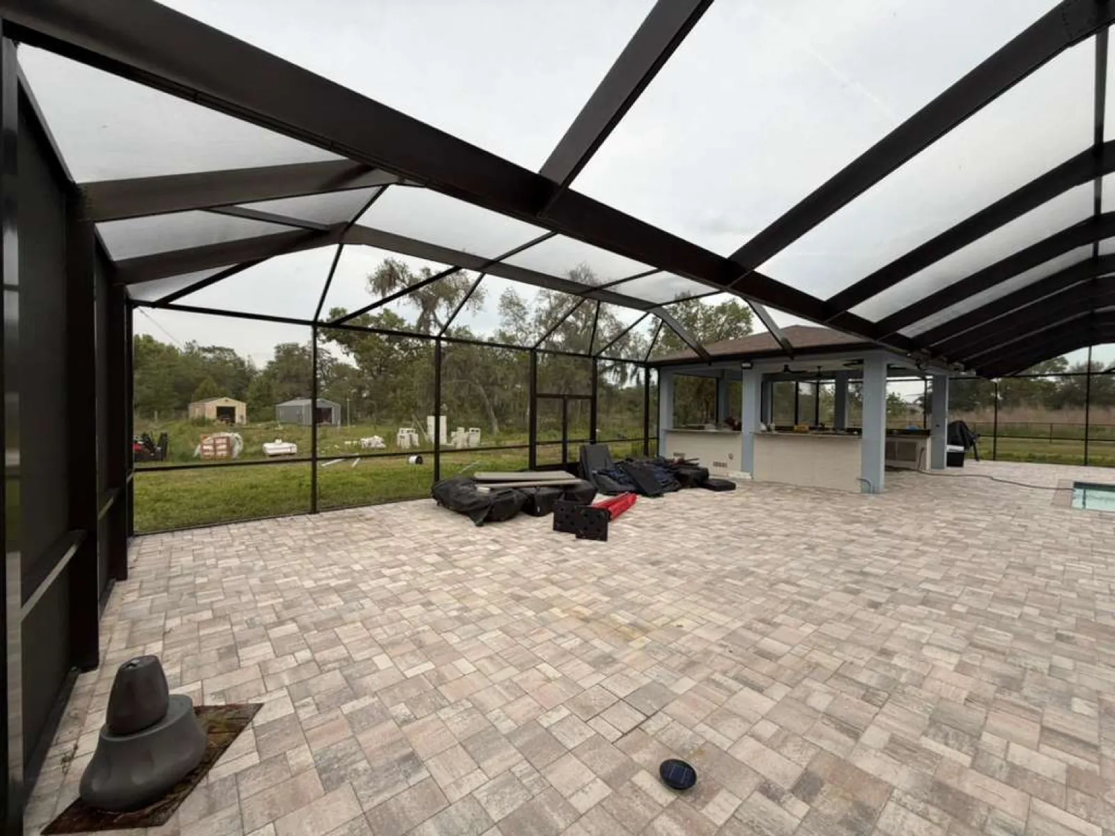 Paver pool deck and outdoor kitchen inside a custom black pool cage in Florida. Built by Top Tier Home Building Solutions (#CGC1527718).