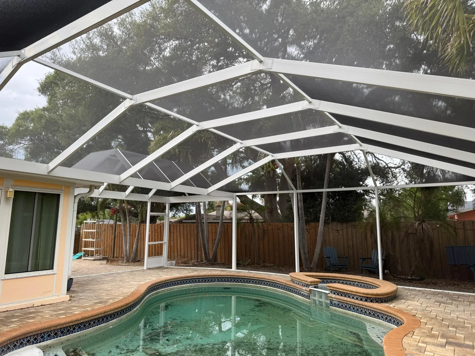 White gable pool cage installed over an existing brick paver pool deck in Florida, showing enclosure posts anchored around the paver surface. Top Tier Home Building Solutions (#CGC1527718).