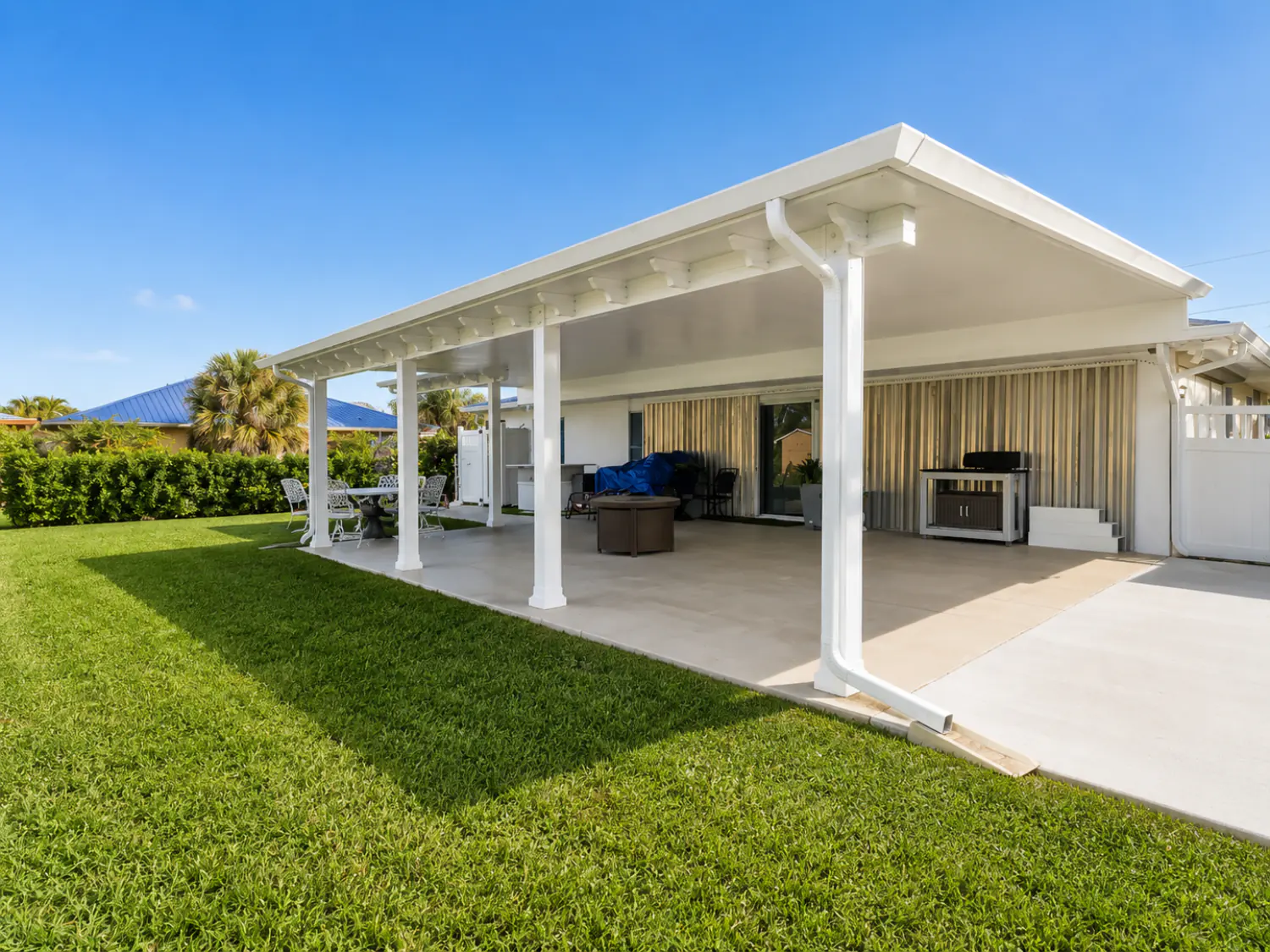 White aluminum pergola with solid roof covering a backyard patio with outdoor kitchen and seating in Florida